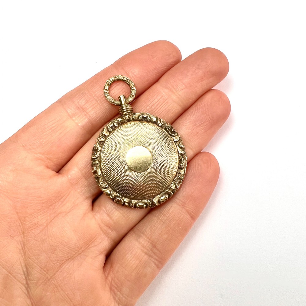 A Victorian 15ct yellow gold oval locket pendant featuring an engine-turned centre, a blank central cartouche, and a chased floral border. View III
