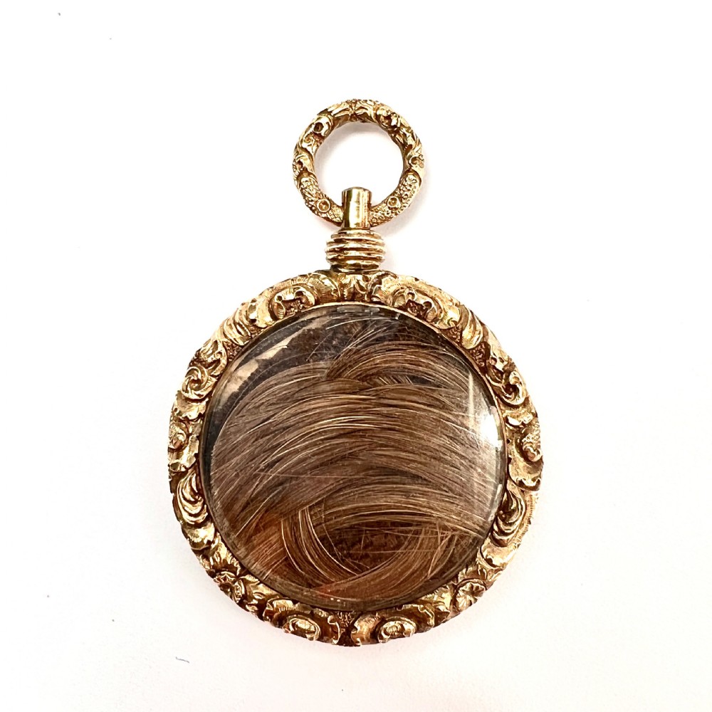A Victorian 15ct yellow gold oval locket pendant featuring an engine-turned centre, a blank central cartouche, and a chased floral border. View IV