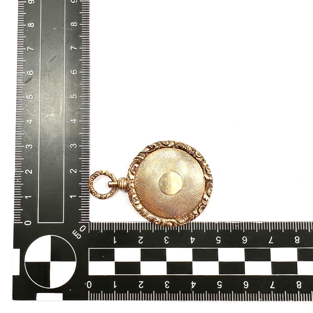 A Victorian 15ct yellow gold oval locket pendant featuring an engine-turned centre, a blank central cartouche, and a chased floral border. View V