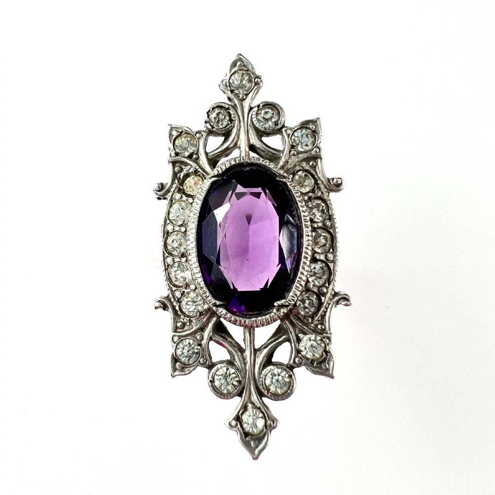 A sterling silver cocktail ring featuring a central oval purple paste stone set within an openwork scroll setting studded with clear paste stones. View II