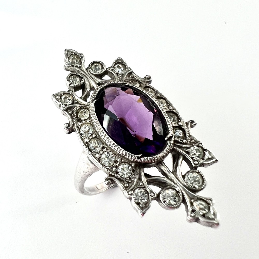 A sterling silver cocktail ring featuring a central oval purple paste stone set within an openwork scroll setting studded with clear paste stones. View III