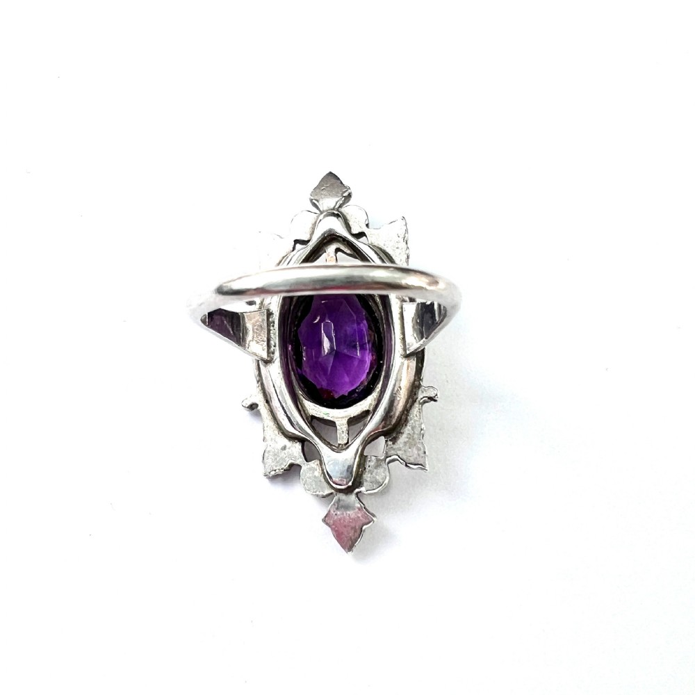 A sterling silver cocktail ring featuring a central oval purple paste stone set within an openwork scroll setting studded with clear paste stones. View VI