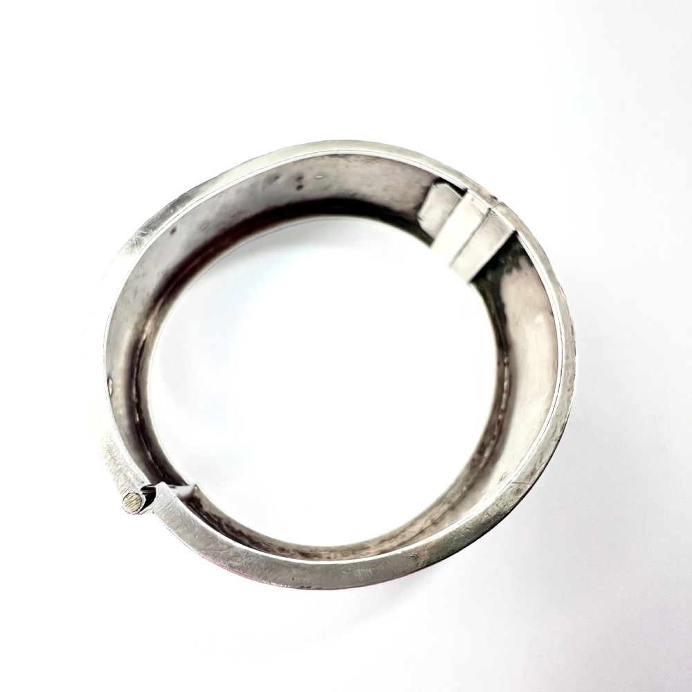A Victorian sterling silver hinged cuff bangle decorated with engraved floral patterns and multi-tone gold overlays, resting on a green fitted presentation box. View VIII