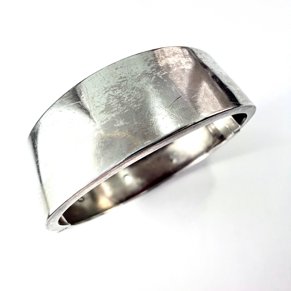 A Victorian sterling silver hinged cuff bangle decorated with engraved floral patterns and multi-tone gold overlays, resting on a green fitted presentation box. View IX
