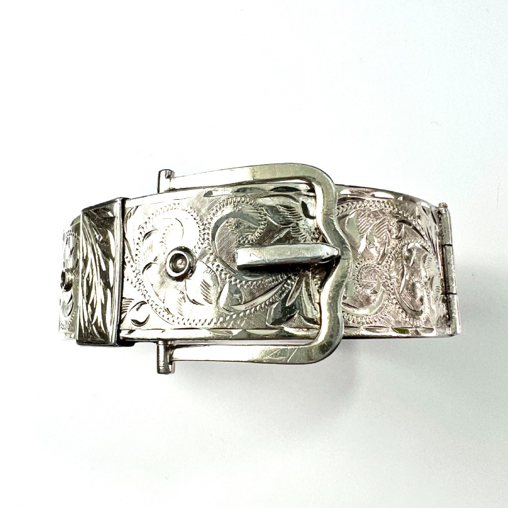 A wide hinged silver buckle bangle decorated with detailed foliate engraved patterns across the front.