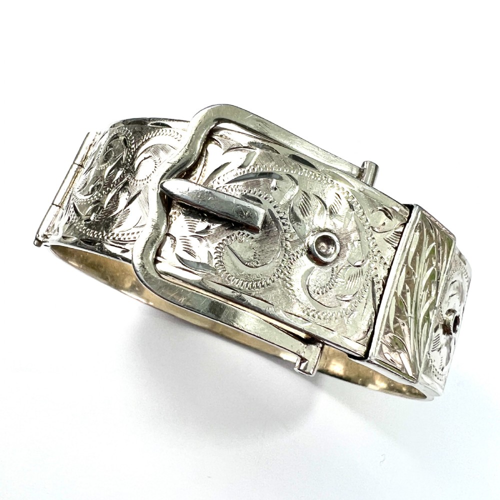 A wide hinged silver buckle bangle decorated with detailed foliate engraved patterns across the front. View II
