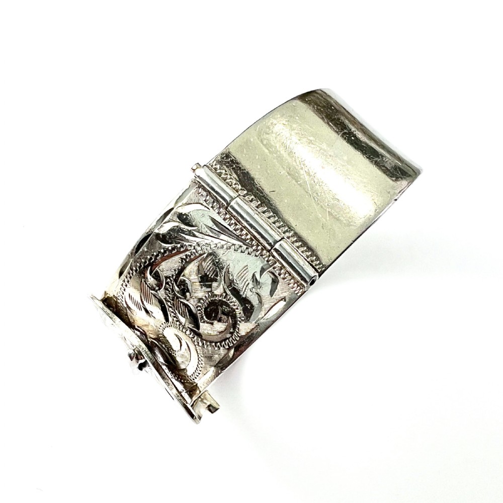 A wide hinged silver buckle bangle decorated with detailed foliate engraved patterns across the front. View III
