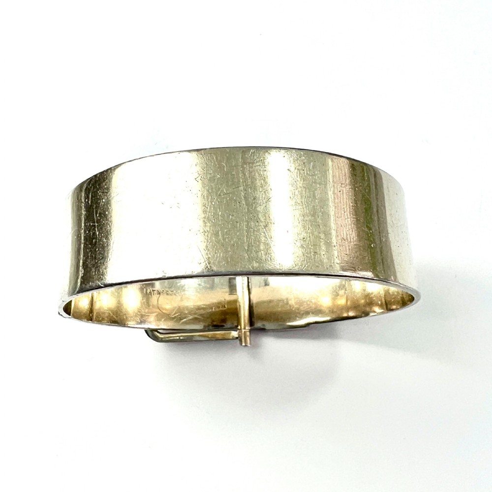 A wide hinged silver buckle bangle decorated with detailed foliate engraved patterns across the front. View V