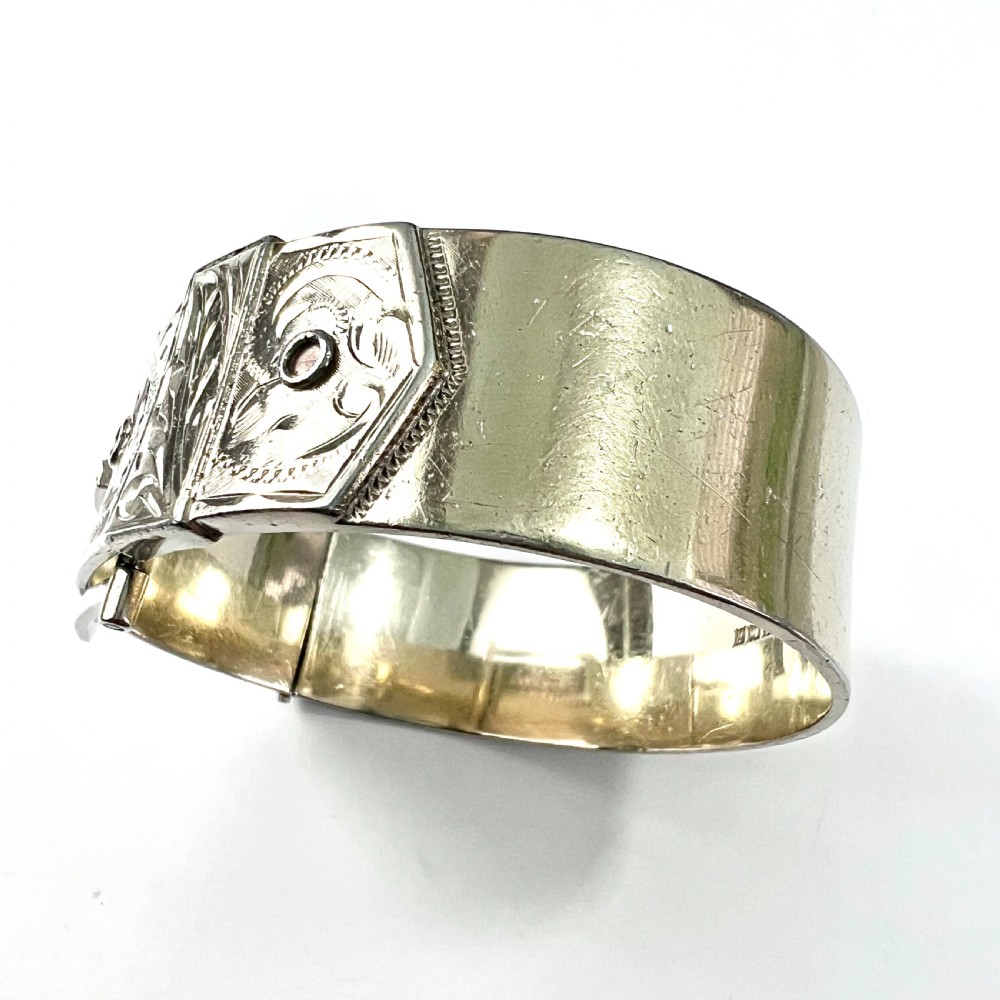 A wide hinged silver buckle bangle decorated with detailed foliate engraved patterns across the front. View VI