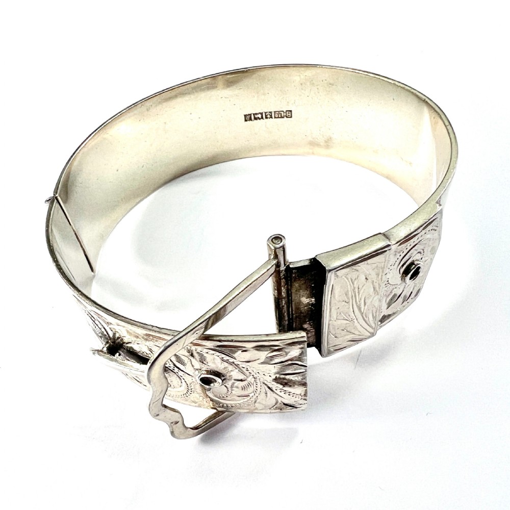 A wide hinged silver buckle bangle decorated with detailed foliate engraved patterns across the front. View VII