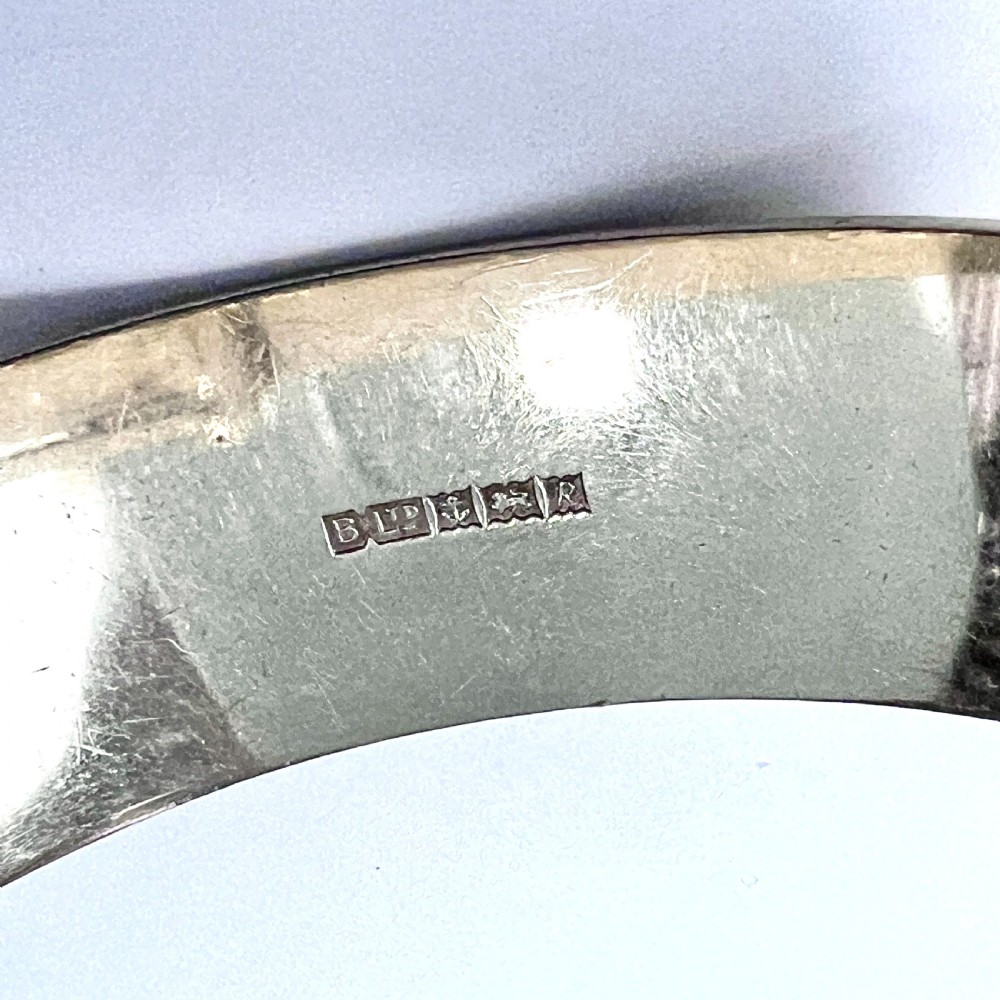 A wide hinged silver buckle bangle decorated with detailed foliate engraved patterns across the front. View IX