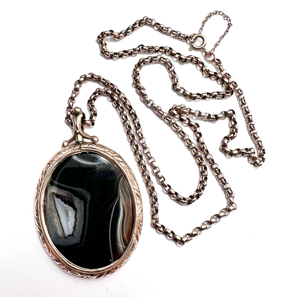 A Victorian 9ct gold oval agate locket with engraved border detailing suspended from a gold chain.