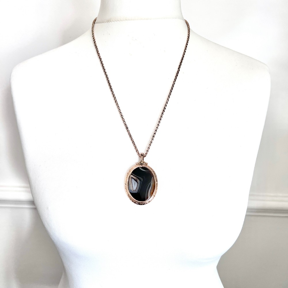 A Victorian 9ct gold oval agate locket with engraved border detailing suspended from a gold chain. View II