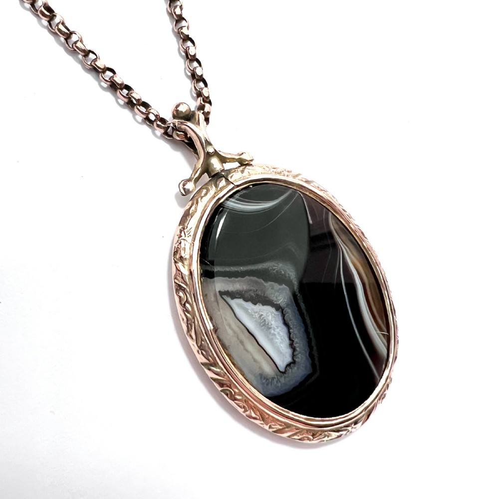 A Victorian 9ct gold oval agate locket with engraved border detailing suspended from a gold chain. View IV