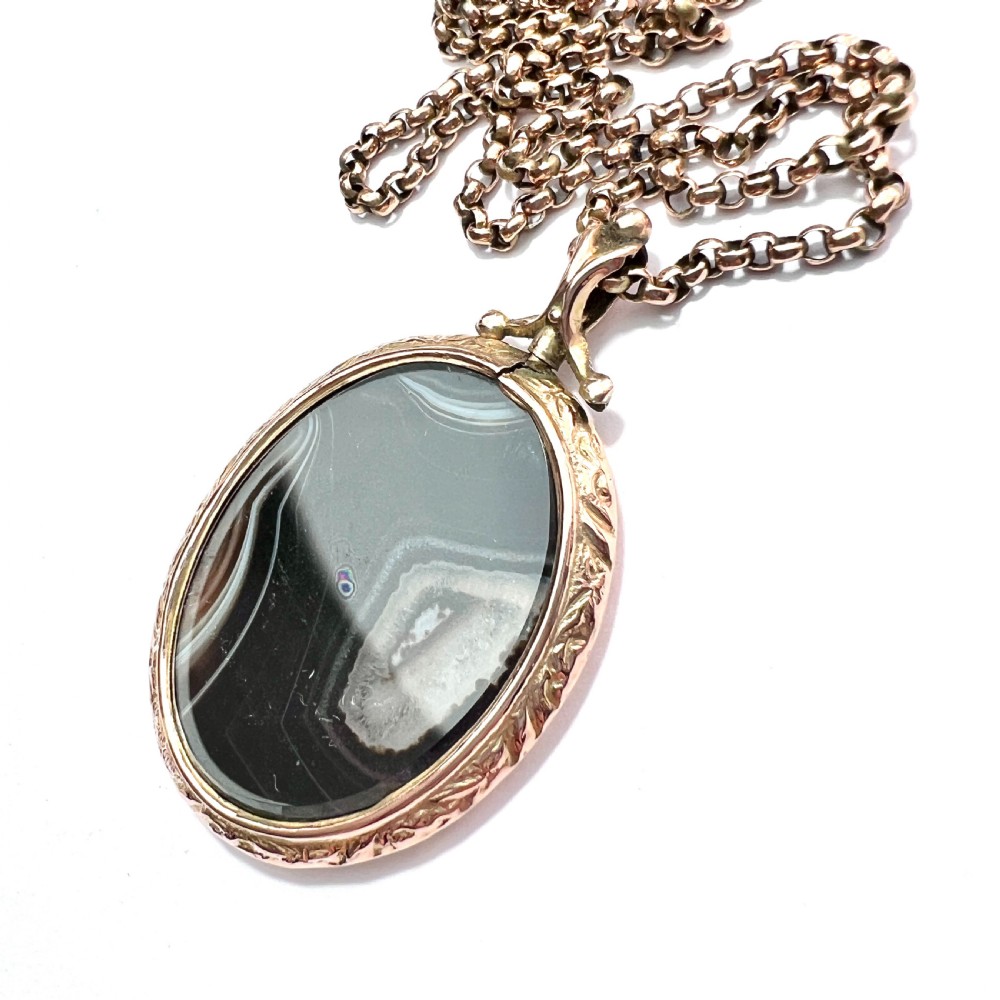 A Victorian 9ct gold oval agate locket with engraved border detailing suspended from a gold chain. View V