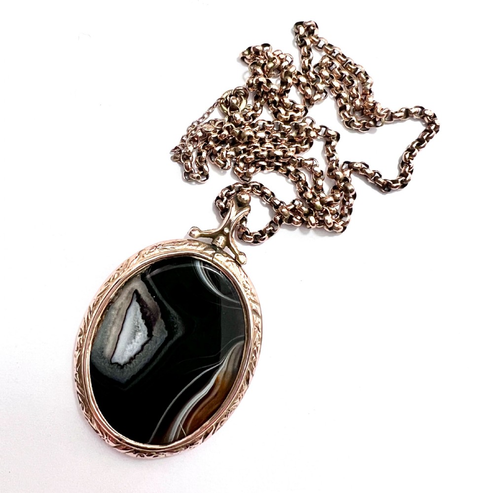 A Victorian 9ct gold oval agate locket with engraved border detailing suspended from a gold chain. View VI