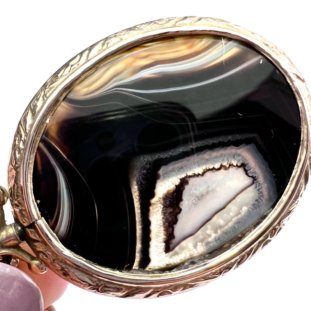 A Victorian 9ct gold oval agate locket with engraved border detailing suspended from a gold chain. View VII