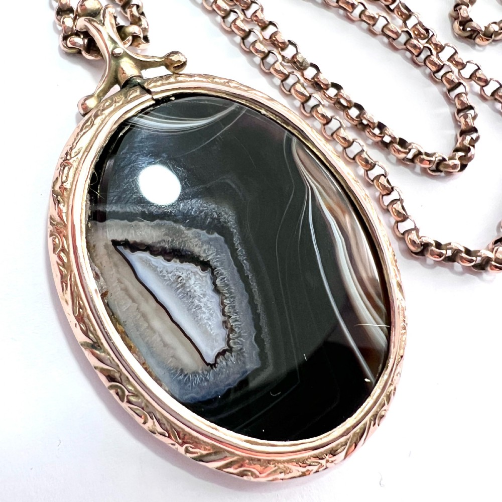 A Victorian 9ct gold oval agate locket with engraved border detailing suspended from a gold chain. View VIII