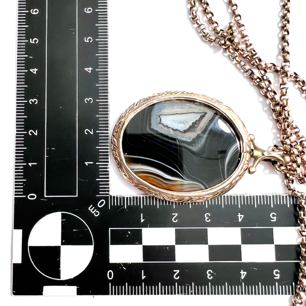 A Victorian 9ct gold oval agate locket with engraved border detailing suspended from a gold chain. View IX
