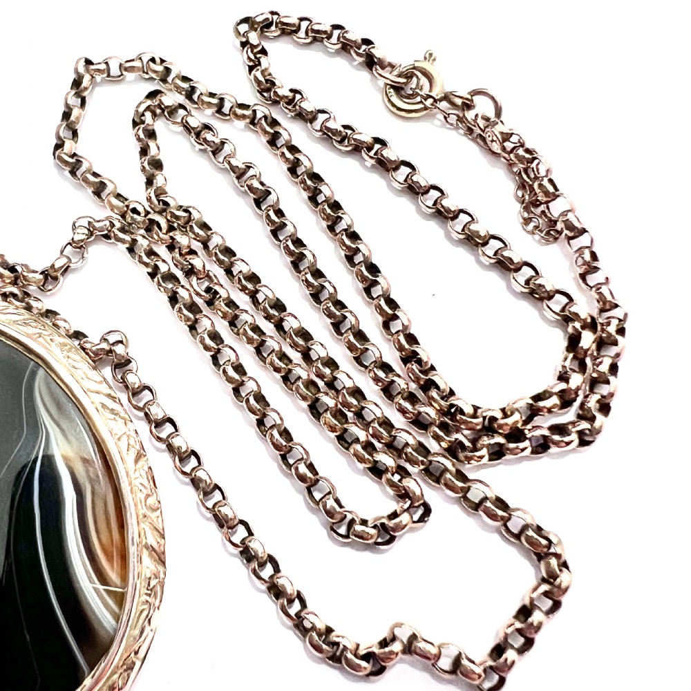 A Victorian 9ct gold oval agate locket with engraved border detailing suspended from a gold chain. View X