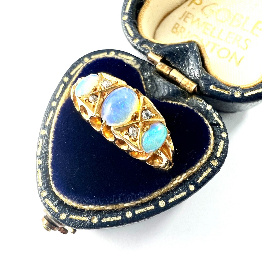 A Victorian 18ct gold ring featuring three cabochon opals separated by diamond accents within a carved scroll setting.