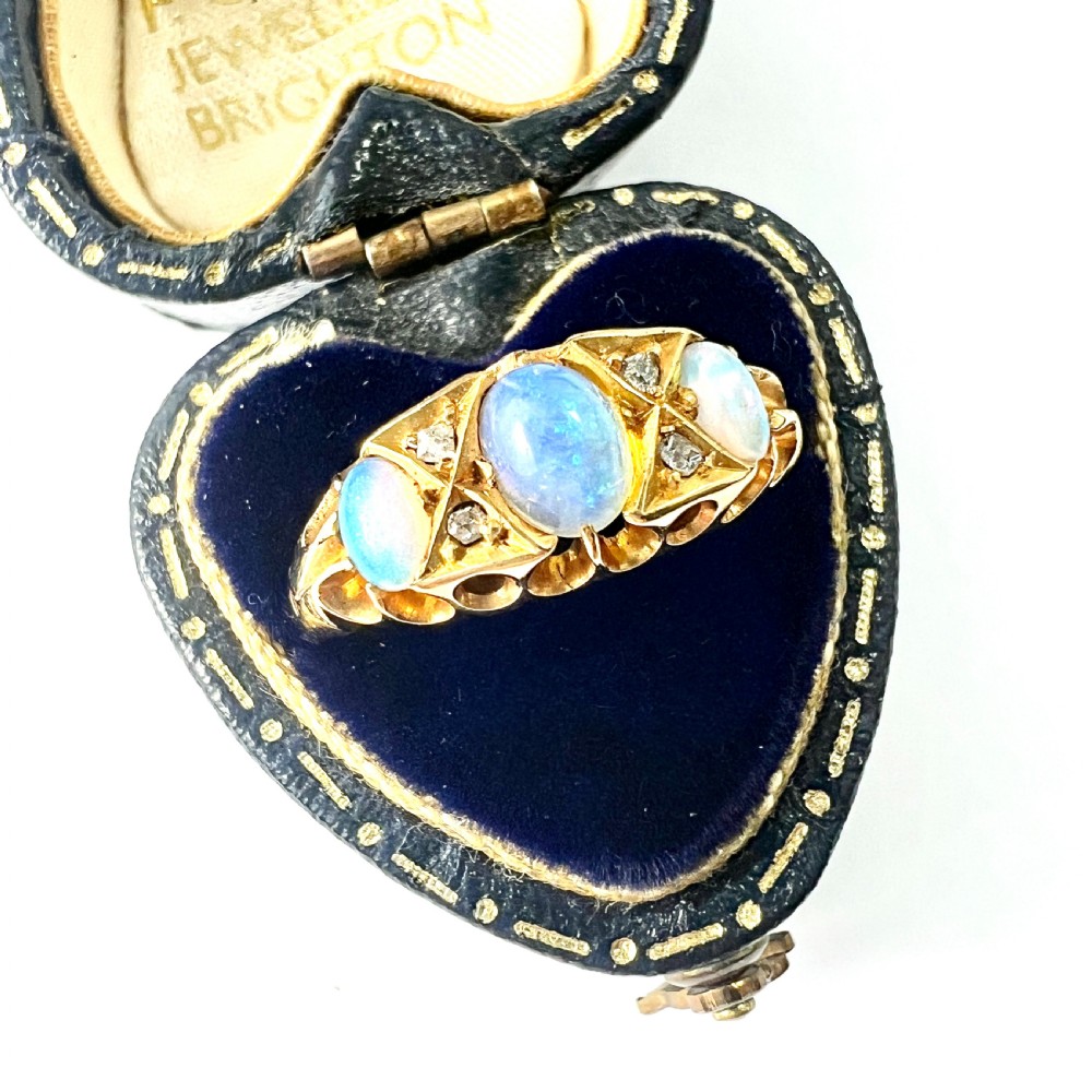 A Victorian 18ct gold ring featuring three cabochon opals separated by diamond accents within a carved scroll setting. View II