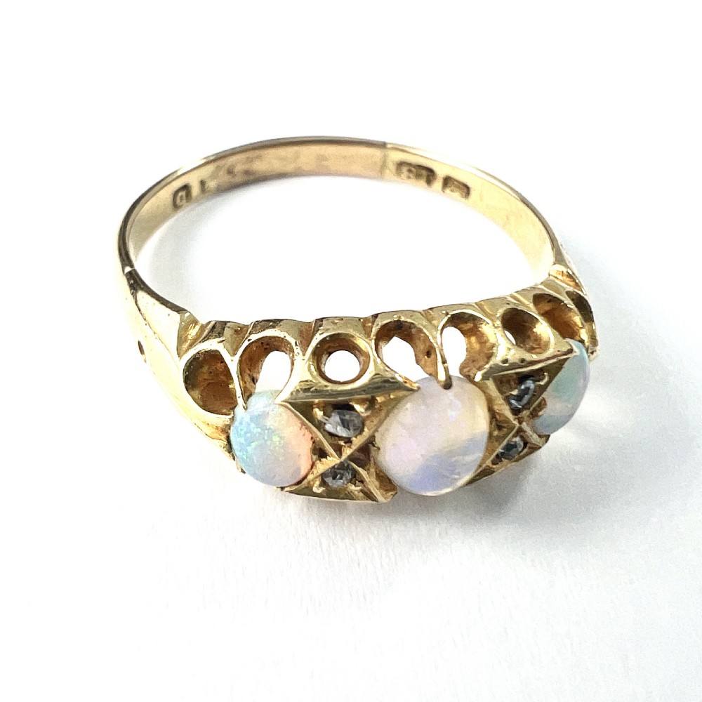 A Victorian 18ct gold ring featuring three cabochon opals separated by diamond accents within a carved scroll setting. View IV