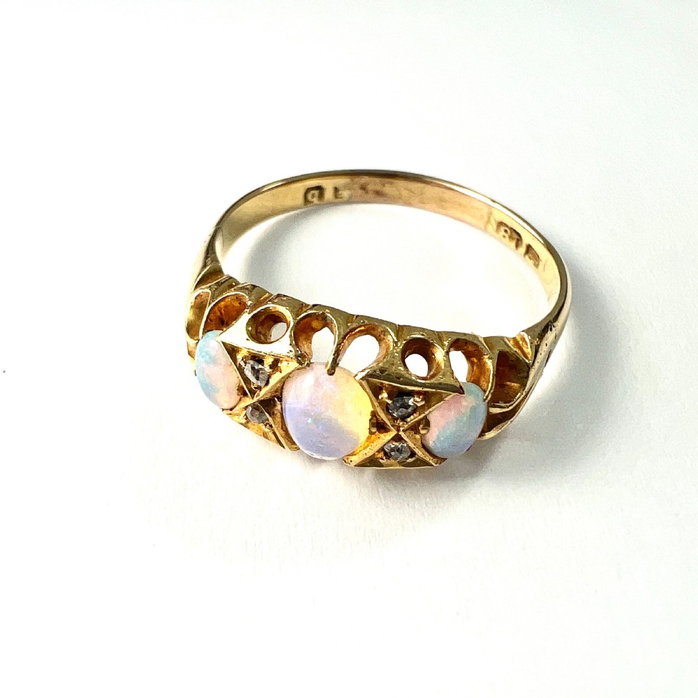 A Victorian 18ct gold ring featuring three cabochon opals separated by diamond accents within a carved scroll setting. View V
