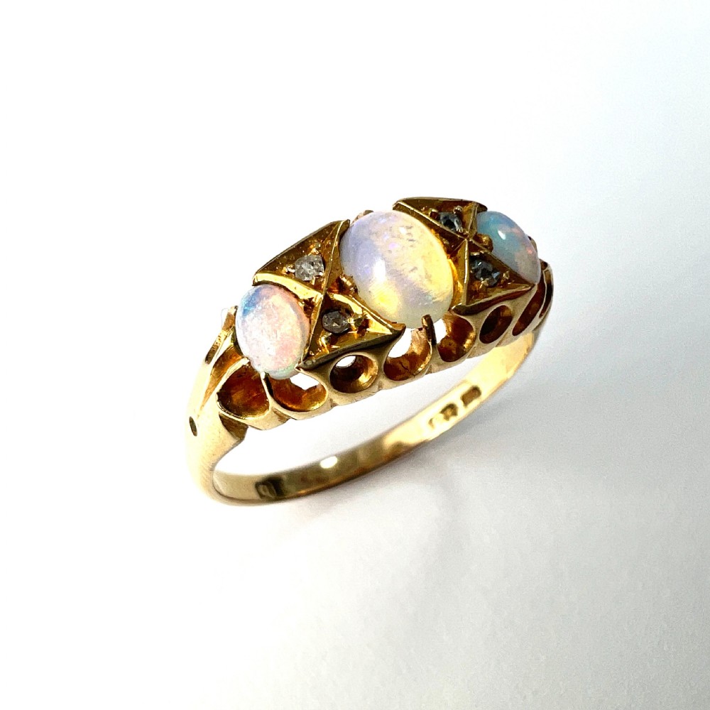 A Victorian 18ct gold ring featuring three cabochon opals separated by diamond accents within a carved scroll setting. View VI