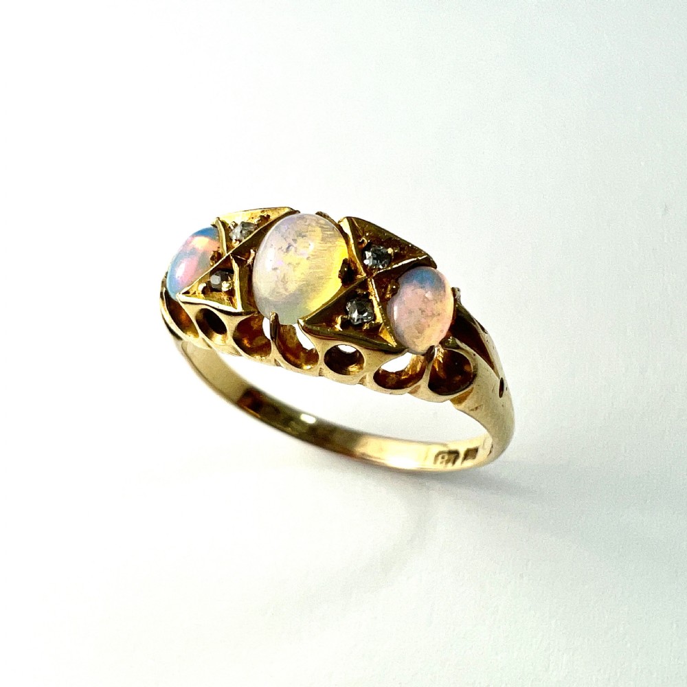 A Victorian 18ct gold ring featuring three cabochon opals separated by diamond accents within a carved scroll setting. View VII