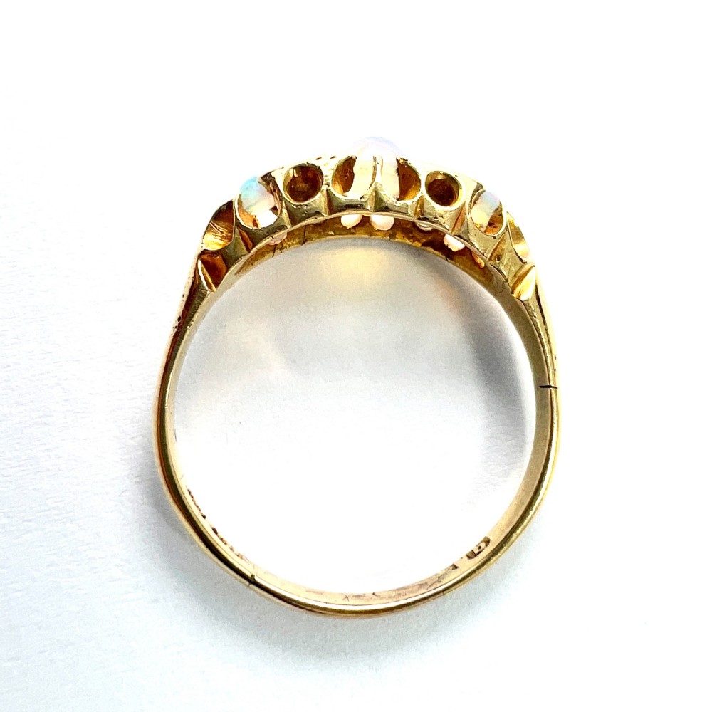 A Victorian 18ct gold ring featuring three cabochon opals separated by diamond accents within a carved scroll setting. View VIII