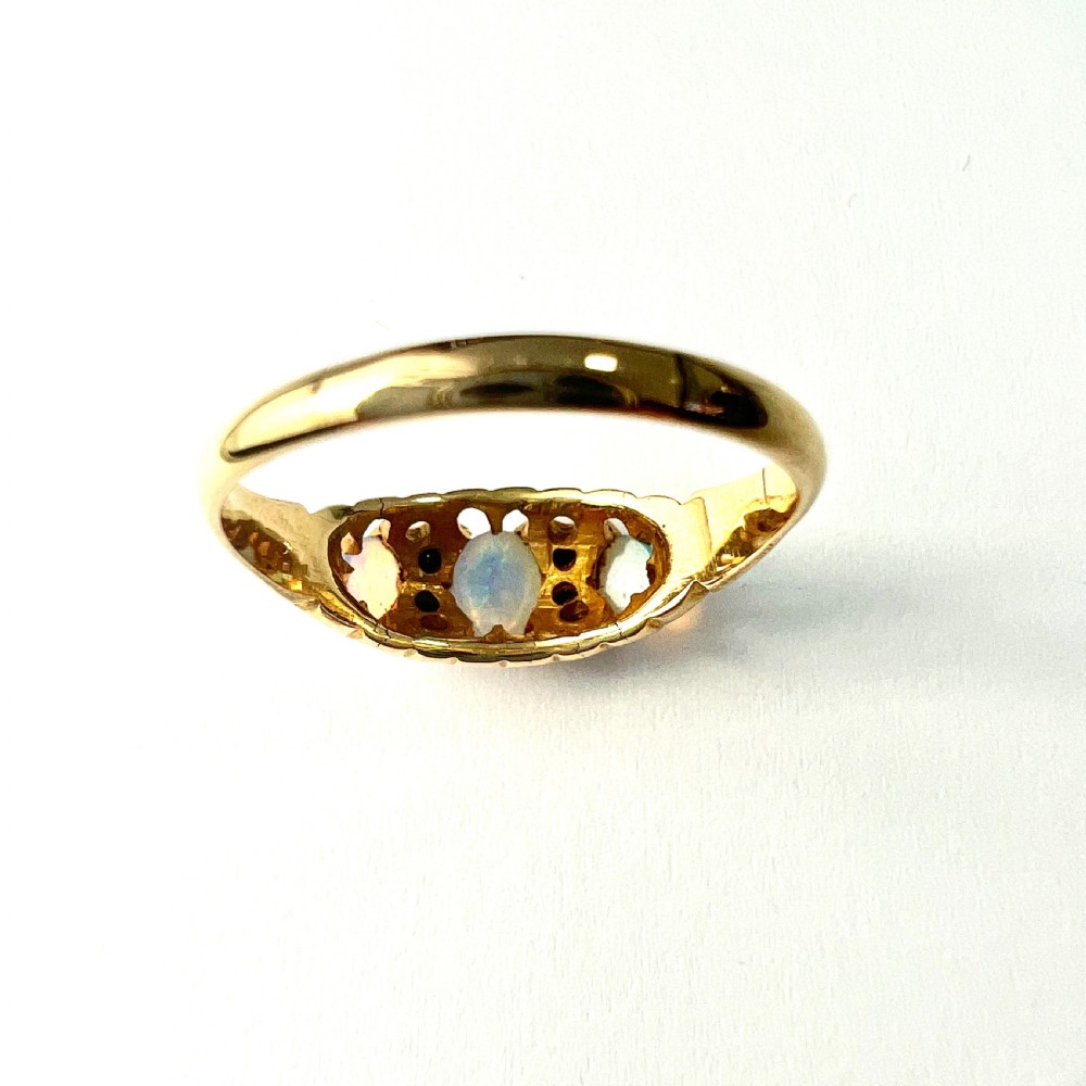A Victorian 18ct gold ring featuring three cabochon opals separated by diamond accents within a carved scroll setting. View IX