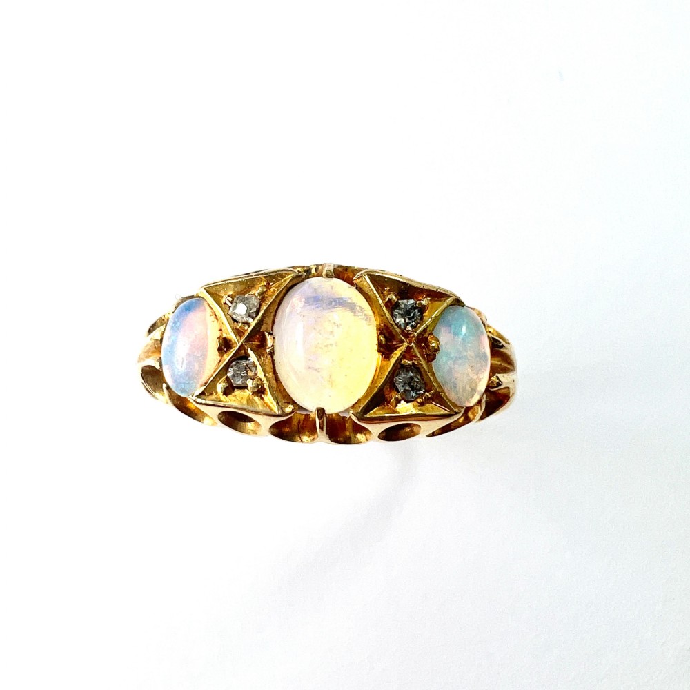A Victorian 18ct gold ring featuring three cabochon opals separated by diamond accents within a carved scroll setting. View XI