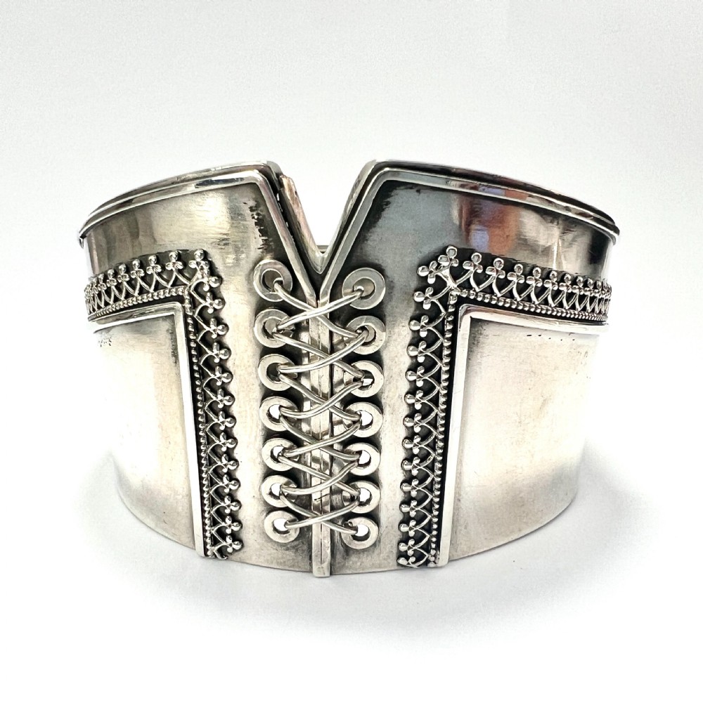 A wide sterling silver hinged cuff bangle featuring a corset-style laced centre detail flanked by intricate filigree borders.
