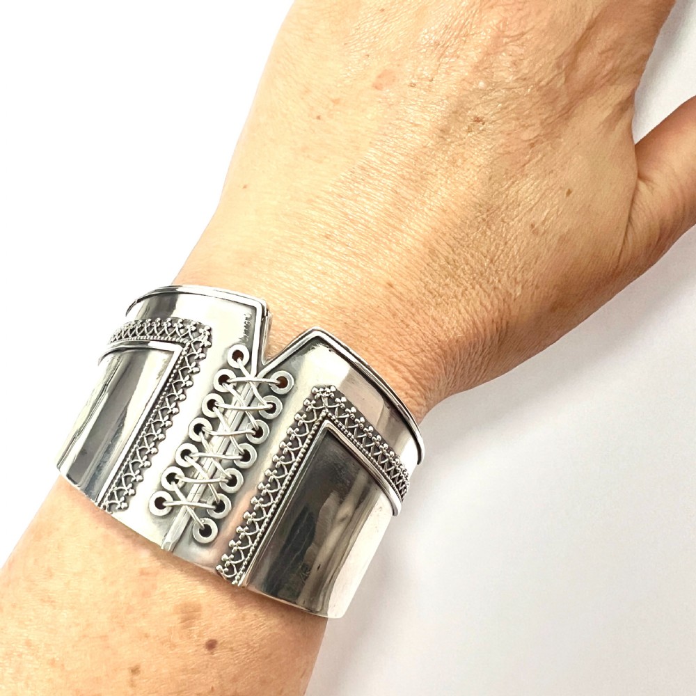 A wide sterling silver hinged cuff bangle featuring a corset-style laced centre detail flanked by intricate filigree borders. View VIII