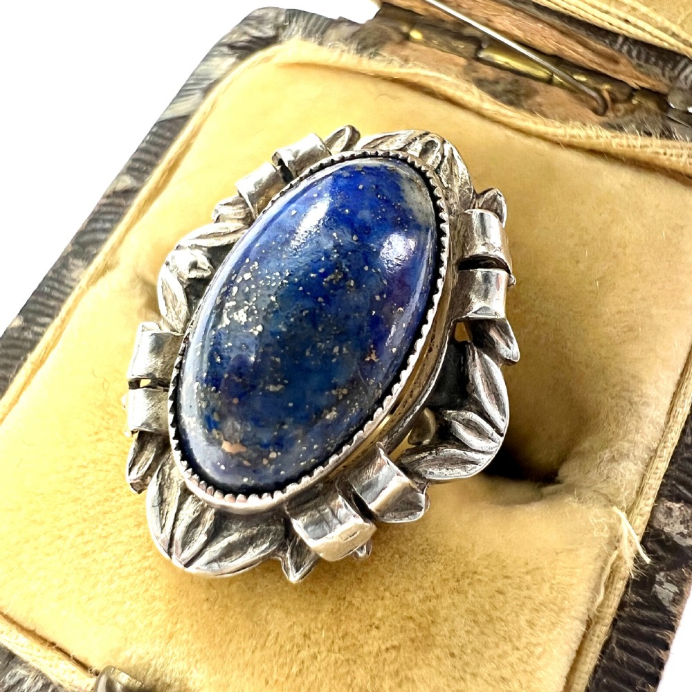 An Arts and Crafts style silver ring featuring a central oval blue lapis lazuli cabochon surrounded by chased silver leaf and ribbon motifs. View II