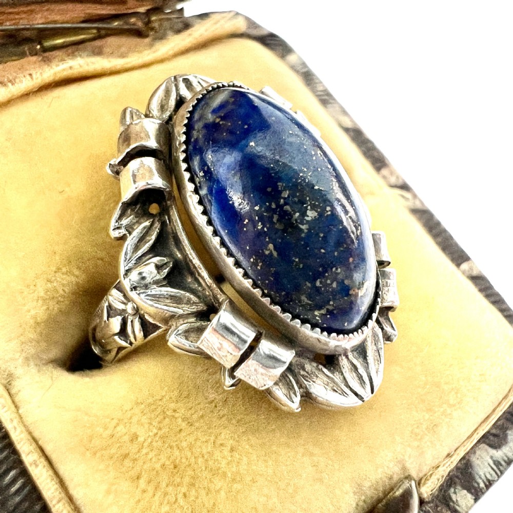 An Arts and Crafts style silver ring featuring a central oval blue lapis lazuli cabochon surrounded by chased silver leaf and ribbon motifs. View III