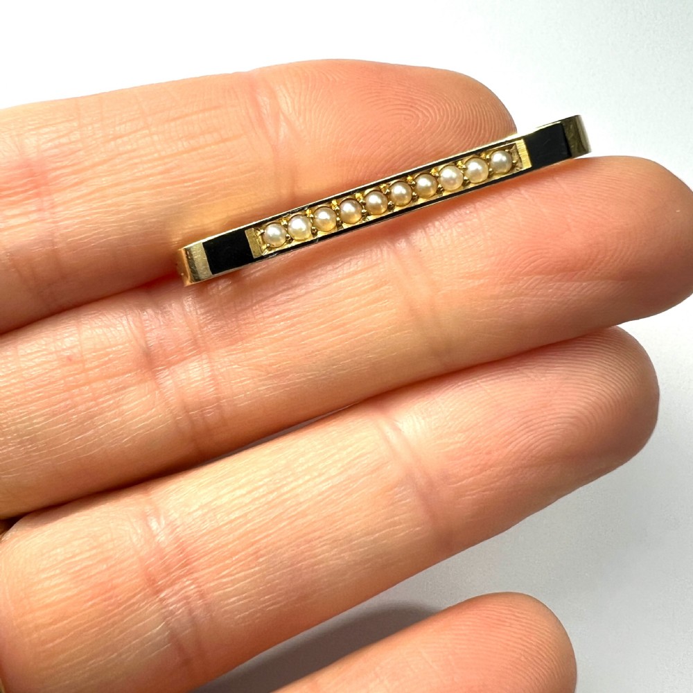 An antique 15ct yellow gold bar brooch designed as a safety pin, set with a row of seed pearls framed by black enamel detailing. View IV