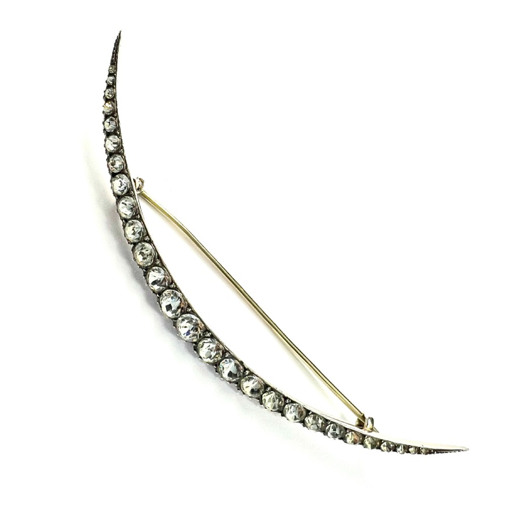 A Victorian crescent moon brooch set with a single row of graduated clear paste stones in a silver setting with a long pin fastening.