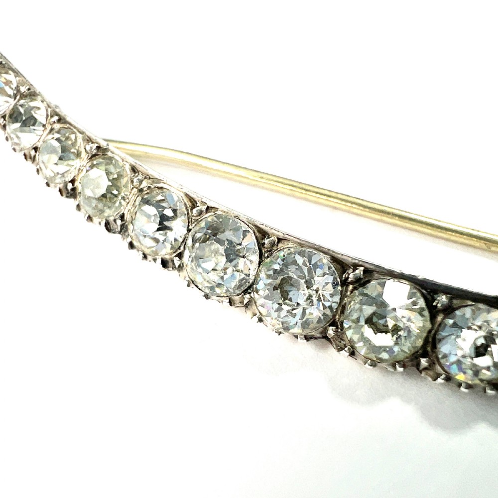 A Victorian crescent moon brooch set with a single row of graduated clear paste stones in a silver setting with a long pin fastening. View II