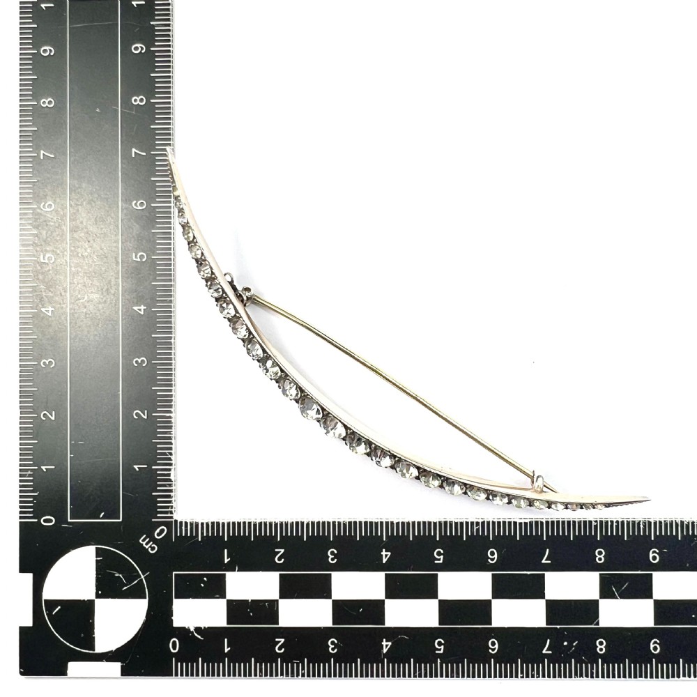 A Victorian crescent moon brooch set with a single row of graduated clear paste stones in a silver setting with a long pin fastening. View V