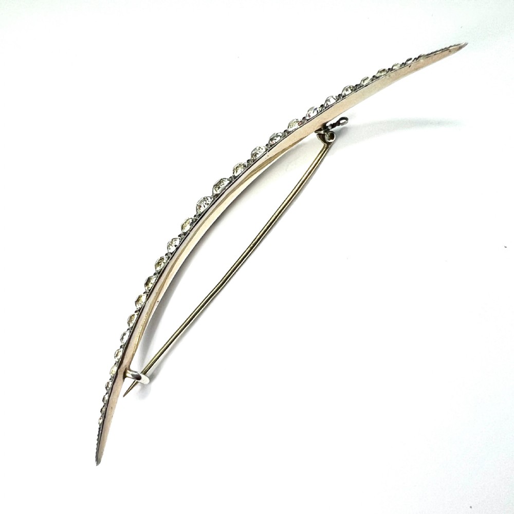 A Victorian crescent moon brooch set with a single row of graduated clear paste stones in a silver setting with a long pin fastening. View VI