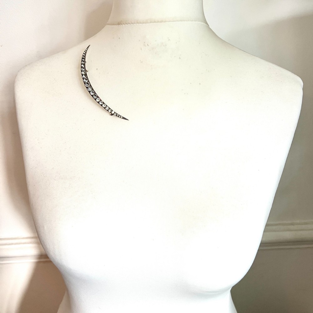 A Victorian crescent moon brooch set with a single row of graduated clear paste stones in a silver setting with a long pin fastening. View VIII