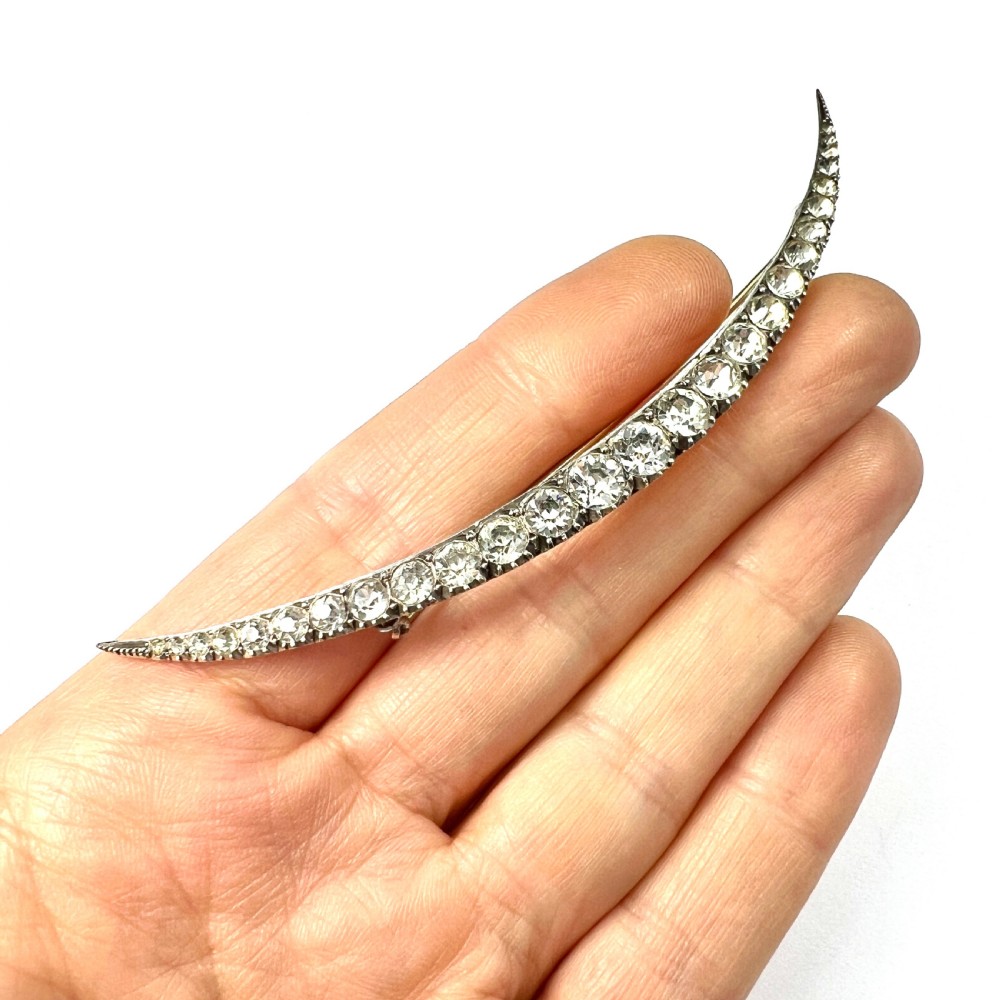 A Victorian crescent moon brooch set with a single row of graduated clear paste stones in a silver setting with a long pin fastening. View IX