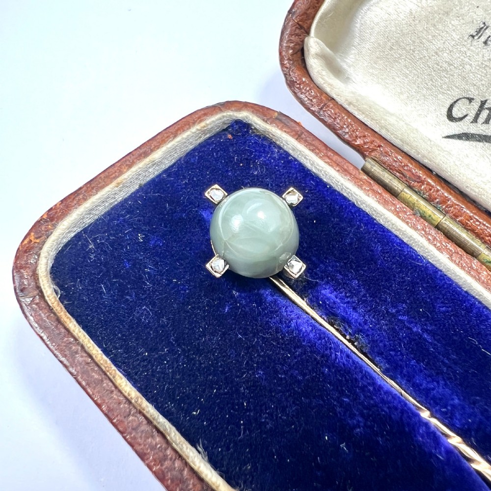 An antique 9ct gold stick pin featuring a central spherical green gemstone set with four small rose-cut diamonds, displayed inside an open velvet-lined leather jewellery box. View II