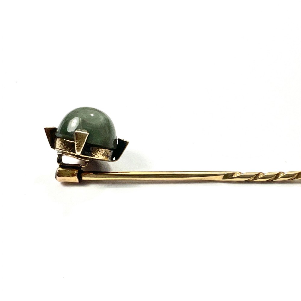 An antique 9ct gold stick pin featuring a central spherical green gemstone set with four small rose-cut diamonds, displayed inside an open velvet-lined leather jewellery box. View V