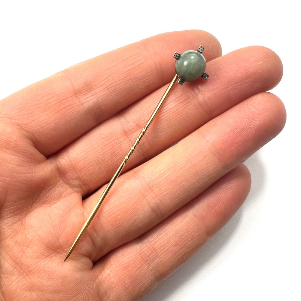 An antique 9ct gold stick pin featuring a central spherical green gemstone set with four small rose-cut diamonds, displayed inside an open velvet-lined leather jewellery box. View VI