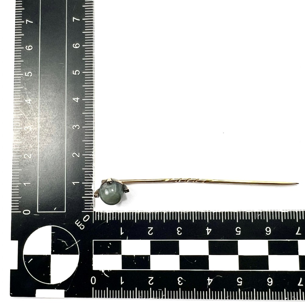 An antique 9ct gold stick pin featuring a central spherical green gemstone set with four small rose-cut diamonds, displayed inside an open velvet-lined leather jewellery box. View VII