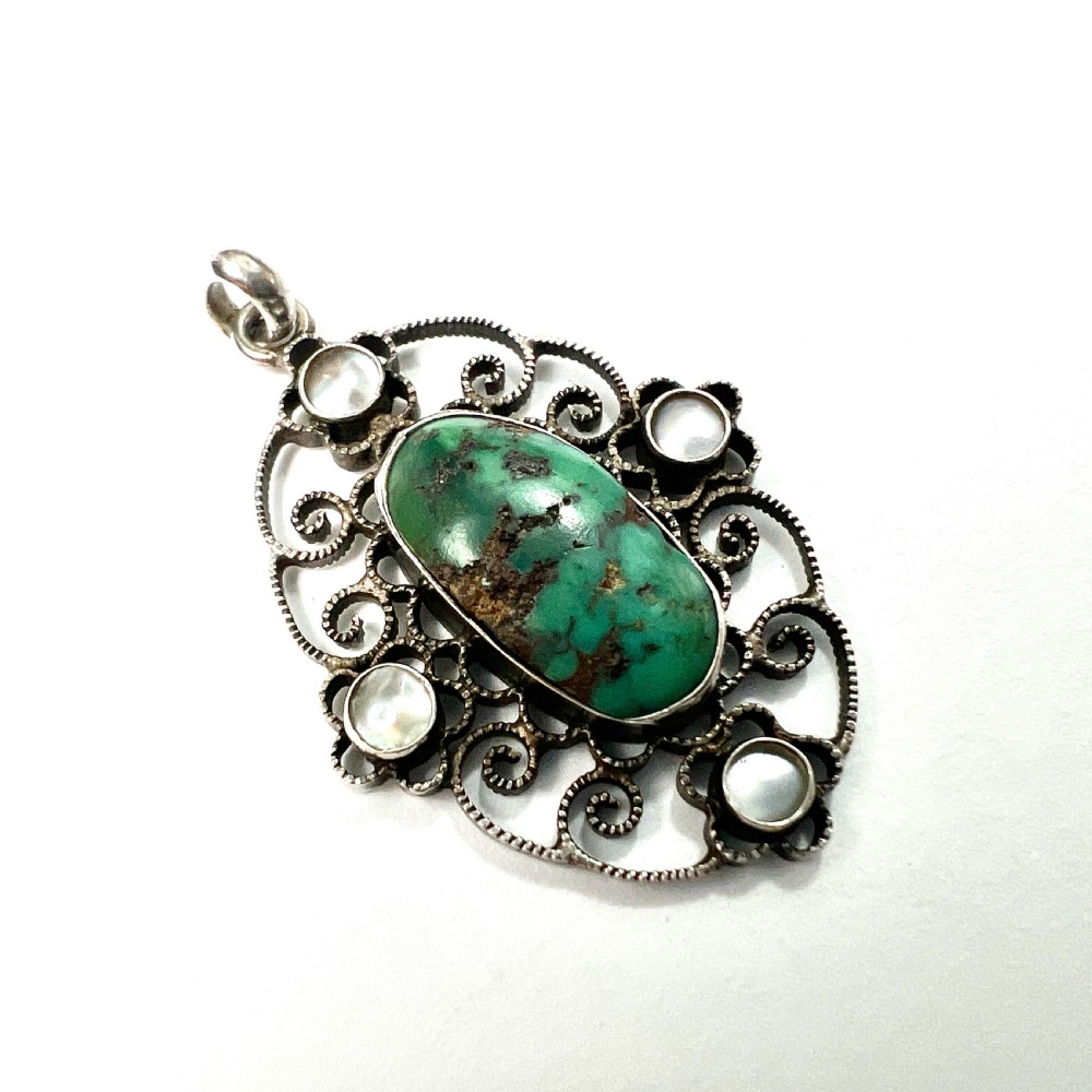 An oval silver pendant featuring an openwork scrollwork design set with a central green turquoise matrix cabochon and four small pearl accents.