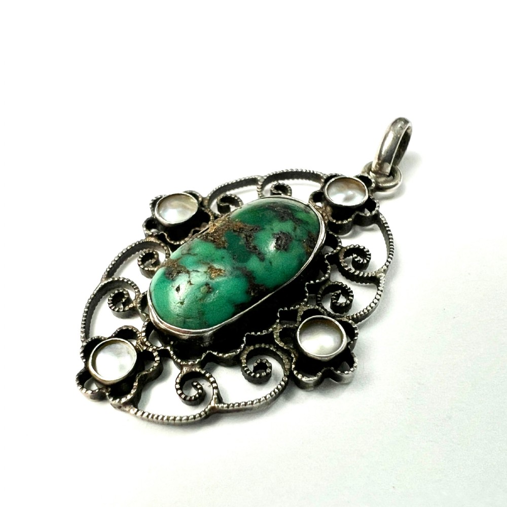 An oval silver pendant featuring an openwork scrollwork design set with a central green turquoise matrix cabochon and four small pearl accents. View III